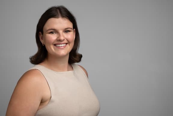 Portrait of Erin Kinghorn, smiling, against a grey studio backdrop